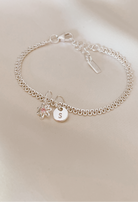 A lace chain bracelet is shown ip close on silk with a beautiful Daisy Pendant taht has a pink cubic zirconia on it and a Petite Initial Pendant.
