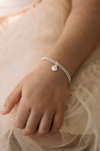Perfectly simple and beautiful.  The Little Mermaid Cuban Link bracelet in child length with a mini shell pendant is worn by a young girl with a peach tulle tutu. 