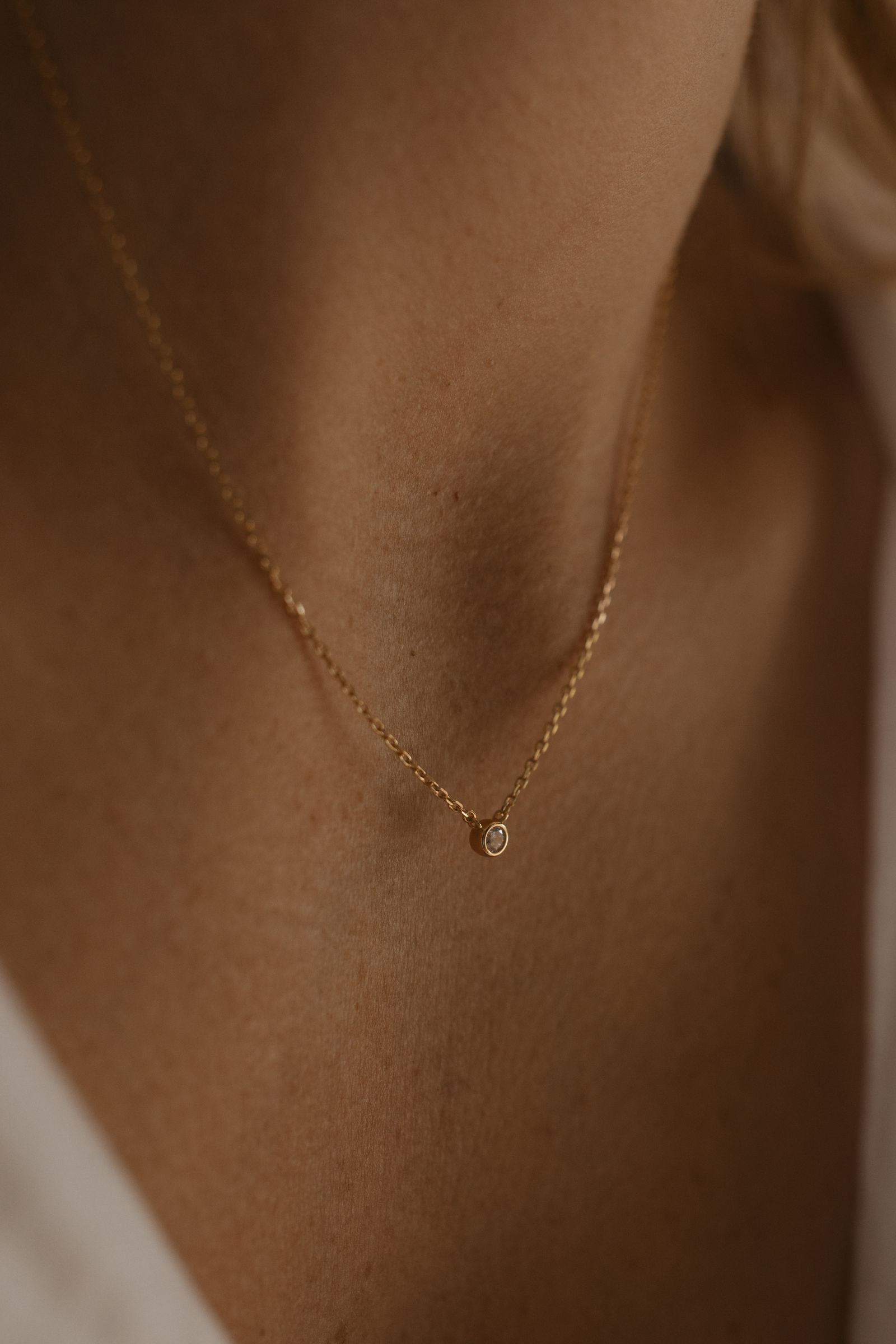 A woman wearing the Lumé Necklace by Bluebird Jewellery, a delicate gold pendant designed to reflect light and celebrate life’s special milestones.