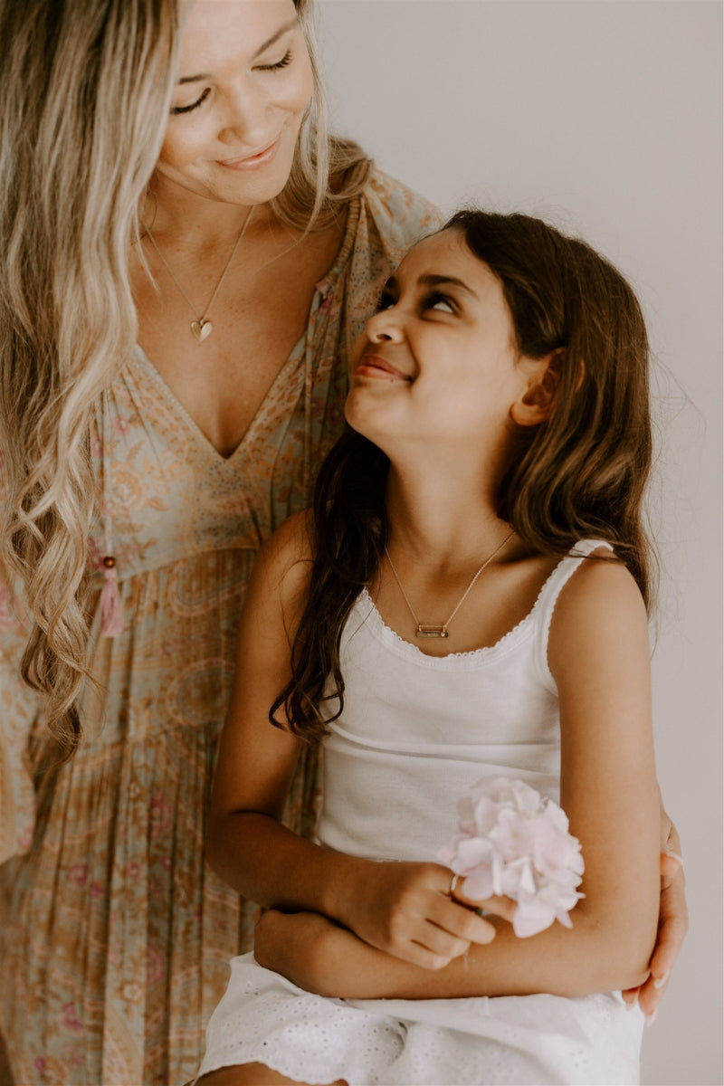 A mother is looking lovingly at her daughter.  Mother and daughter are wearing matching Darling Necklaces.