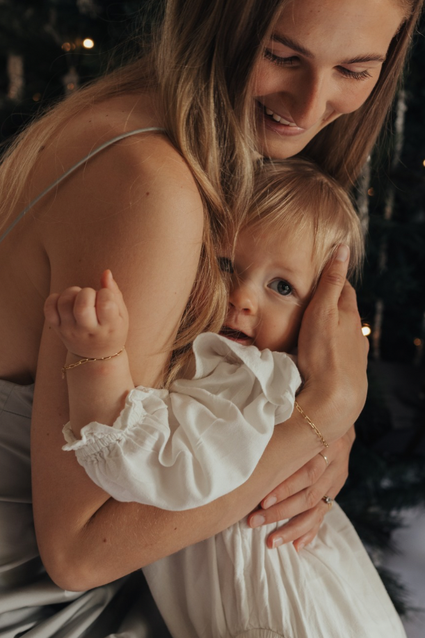 Woman holding a baby in front of a decorated Christmas tree