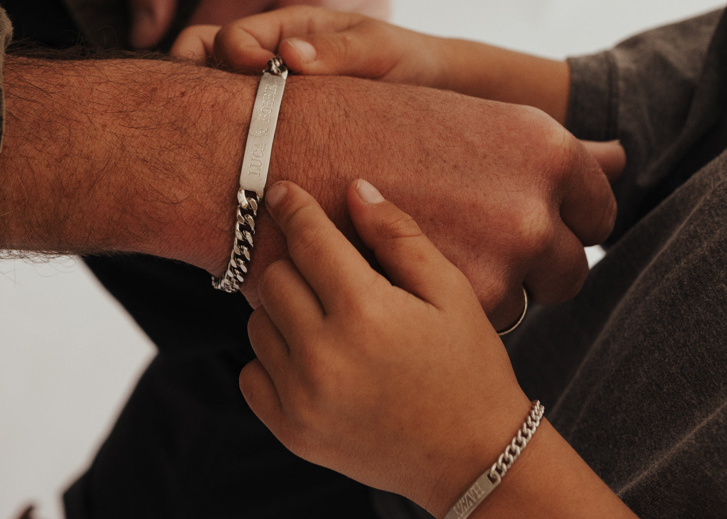 Close-up of two people's hands with bracelets on a neutral background