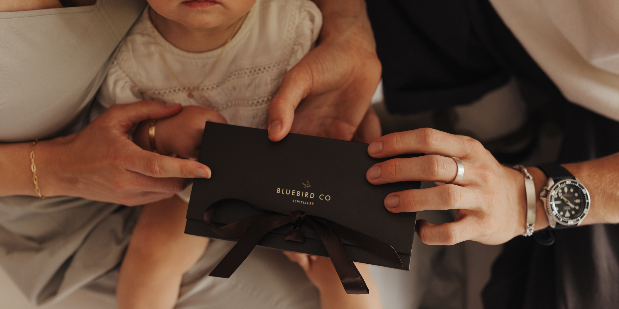 A father holding a gift box.  He is wearing a signature ring and a men's id bracelet