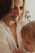 A woman holding her child is wearing a Fob Necklace in Gold