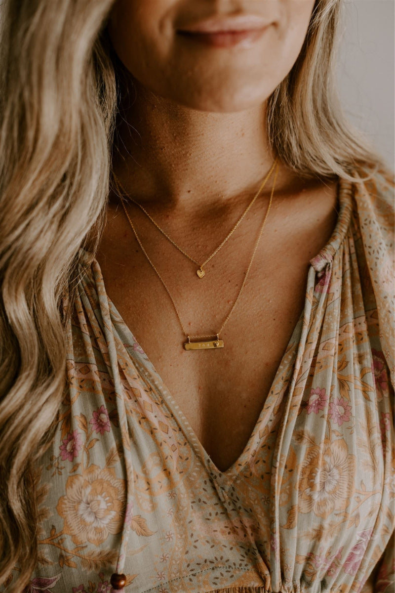 A mother wears the Petite Darling Necklace layered with the Darling Bar Necklace that has personalised with engraving on the bar pendant. 