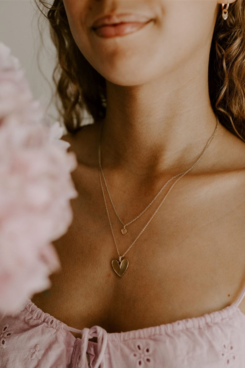 A beautiful side angle of the Petite Darling Necklace worn by a teenage girl. The petite heart shaped pendant rests on a fine cable chain necklace and is a timeless necklace.