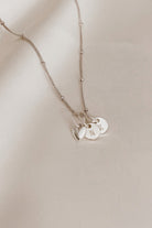 A sterling silver necklace chain with a heart pendant and two petite initial pendants that are round.