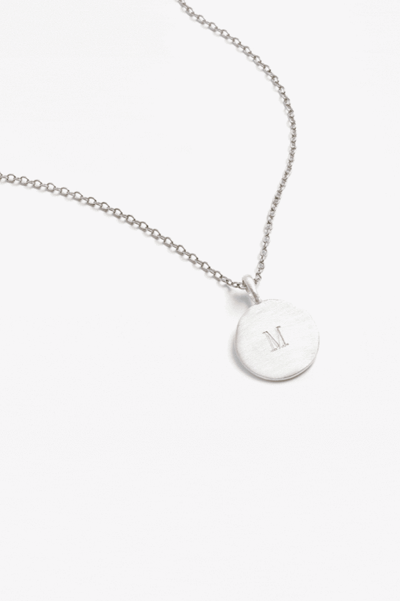 Personalised silver disc necklace with engraved initial M, designed for everyday wear and timeless simplicity.