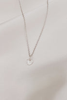 A Petite Darling Necklace is shown on silk with its fine cable chain and uniquely textured surface with raised edges, this petite heart shaped pendant is timeless and stylish and can be personalised by adding Initial Pendants to the chain.