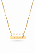 A Bluebird gold bar necklace with a rectangular pendant engraved with the name 'MADDIE' and a small pink heart, suspended from a delicate gold chain on a white background.