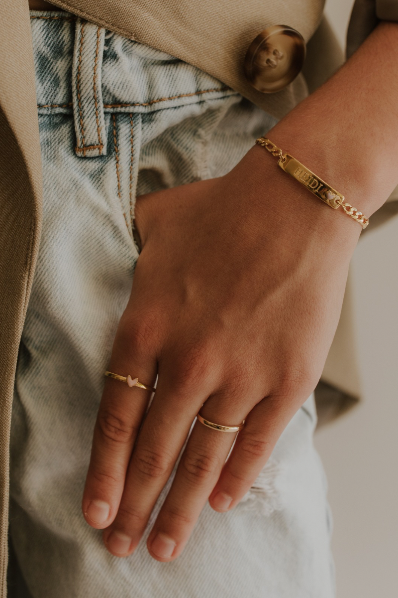 A close-up of a woman's wrist adorned with the Pink Darling Bracelet by Bluebird Jewellery, featuring a soft pink heart pendant and elegant chain with matching darling ring and signature ring. 