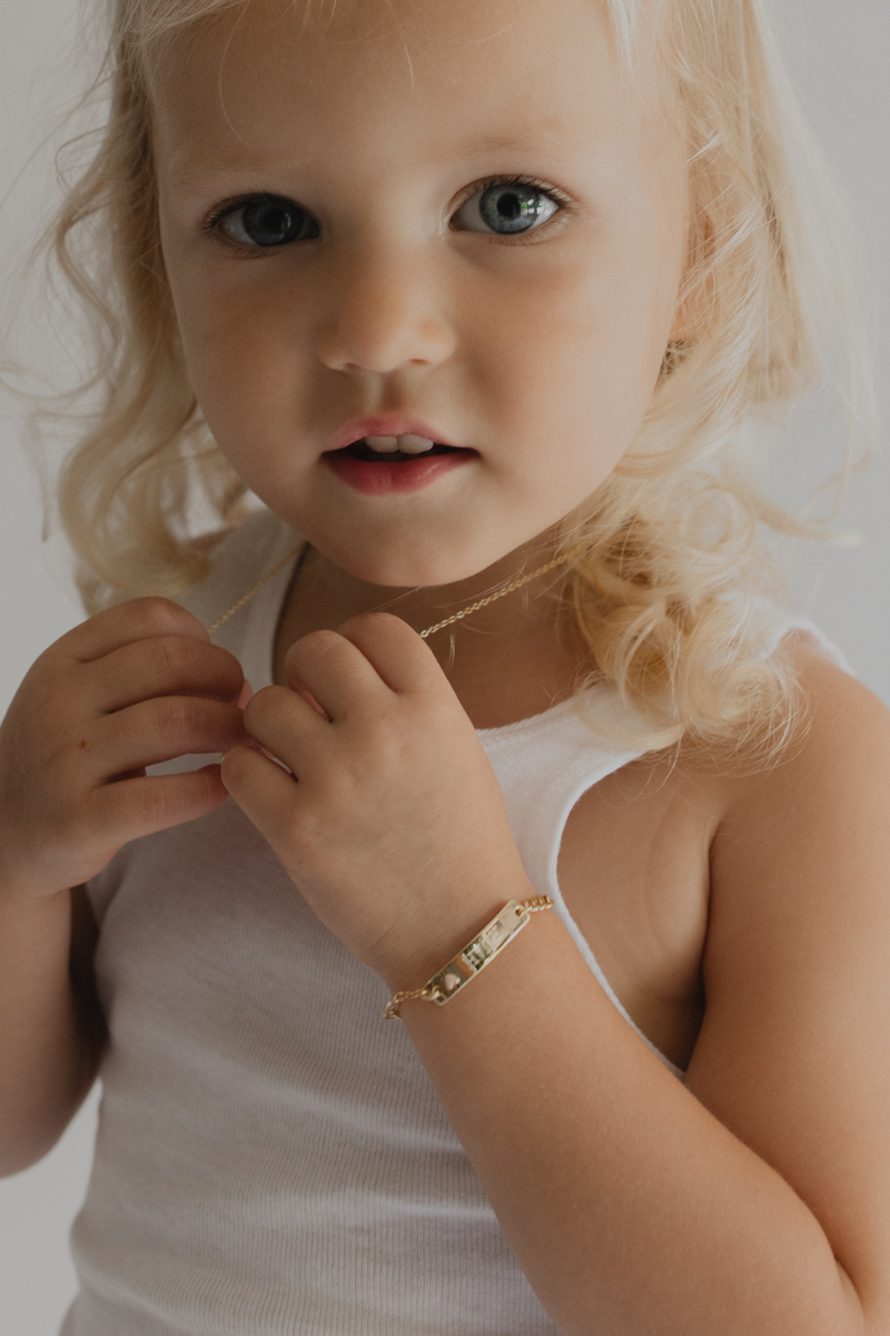 A young girl is wearing a personalised ID bracelet with her name engraved on the front of it with a pink petite darling necklace.