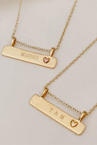 A Pink Darling Bar Necklace sits alongside a Darling Bar Necklace.  Both necklaces have personalised engraving on the front of them.