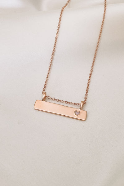 Pink Darling Bar Necklace in rose gold.  A smooth bar pendant necklace that is engravable and features a small pink heart at the end of the bar pendant
