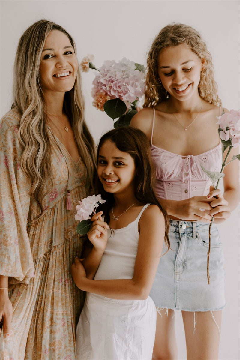 A young girl is wearing the personalised Pink Darling Bar Necklace and her mum and sister are wearing other Darling Necklaces.