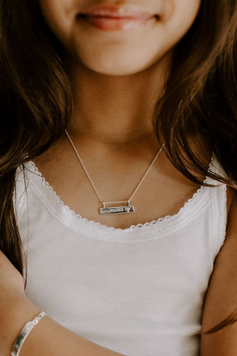 A young girl is wearing the Pink Darling Bar Necklace and has a name engraved on it.