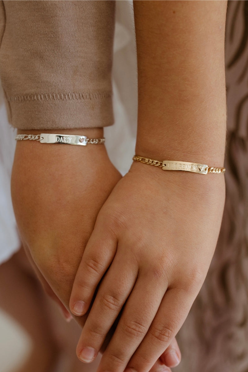 Two friends are holding hands and wearing matching friendship bracelets with personalised engraving on them.