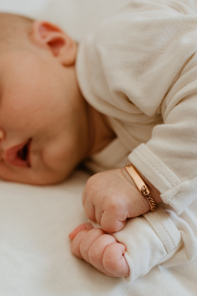 A close up of a small newborn child wearing the Pink Darling Bracelet in Rose Gold Vermeil.  The bracelet features an engravable bar pendant and is a beautiful keepsake gift.