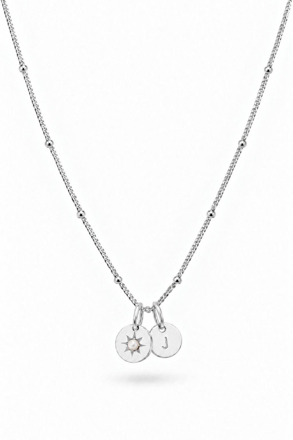 A silver beaded chain necklace with two small round pendant charms, one engraved with a sunburst and the other with the letter 'J', shown on a plain white background.