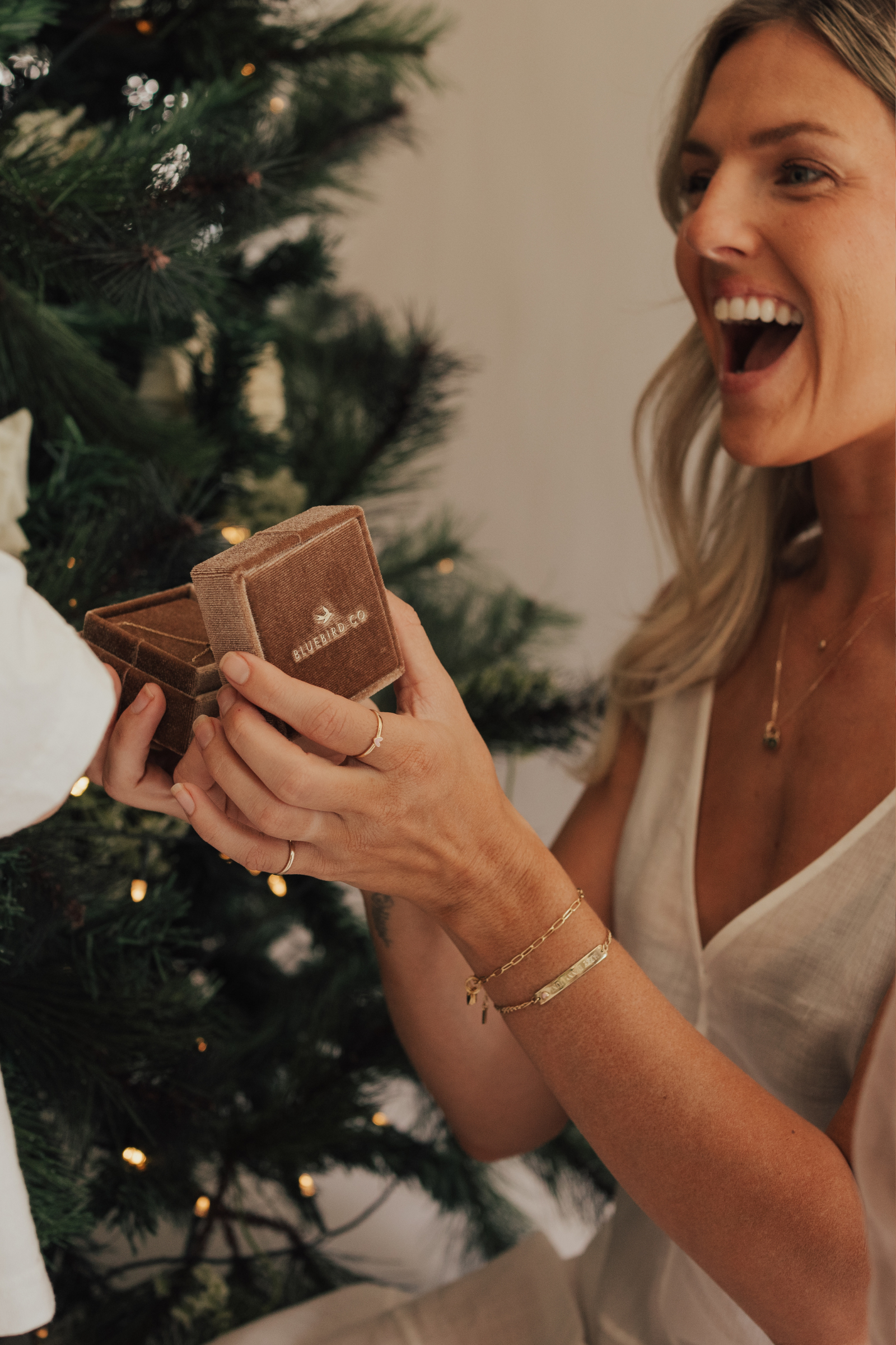 A mother wearing the Posie and Pink Darling bracelets and fine minimalist rings, captured holding a velvet jewellery box and radiating happiness by Bluebird Jewellery.