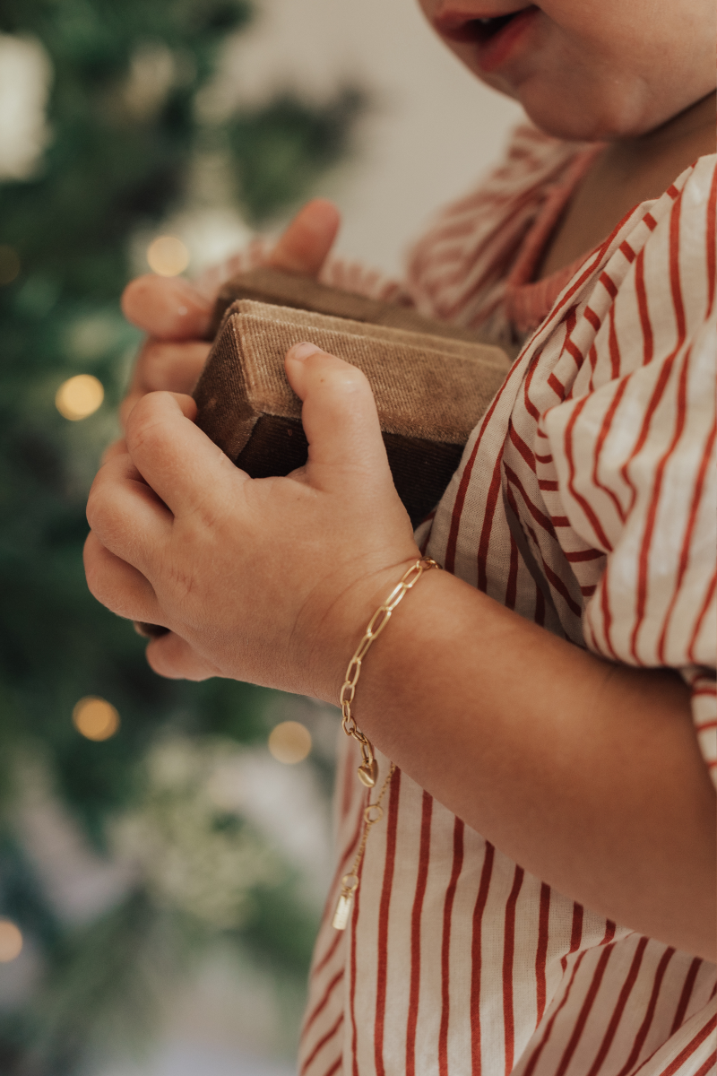 A baby is wearing a Posie Bracelet with a Mini Sweetheart pendant on it.