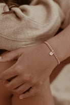 A refined image of a woman’s wrist wearing a rose gold Cuban Link Chain and solid gold rectangular pendant, photographed in natural light by the seaside.