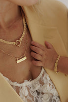 A mother is wearing the Signature Bar necklace in gold vermeil with the word 'MAMA' engraved on the front of it.  It is layered with the Signature Statement Necklace and matches her daughter's Signature Bracelet.