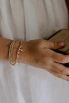 A young girl is wearing both the Cuban Link Bracelet with a Daisy Pendant and the Signature Bracelet with her name engraved on it.  The two bracelets compliment one another.