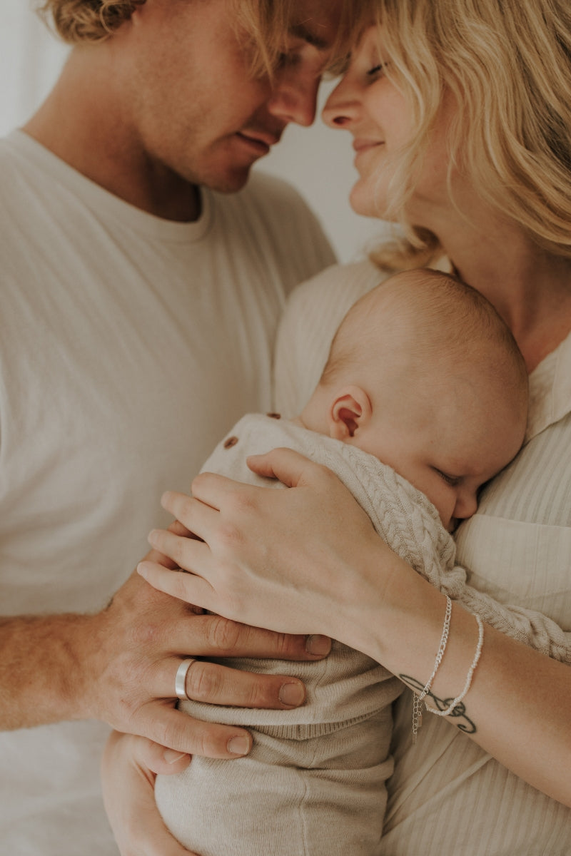 A husband and wife are hugging their newborn son and the father is wearing his Signature Men's Ring.  The ring is engraved with his wife and son's names inside it.