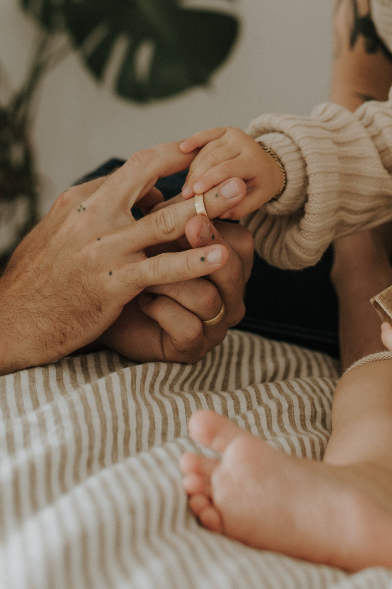 A young girl is putting a solid gold Signature Men's Ring on her dad's finger whilst she also holds onto the velvet ring box.