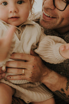 A young girl is looking into the camera as her father smiles at her and holds her.  He is wearing his Solid Gold Signature Men's Ring on his ring finger.