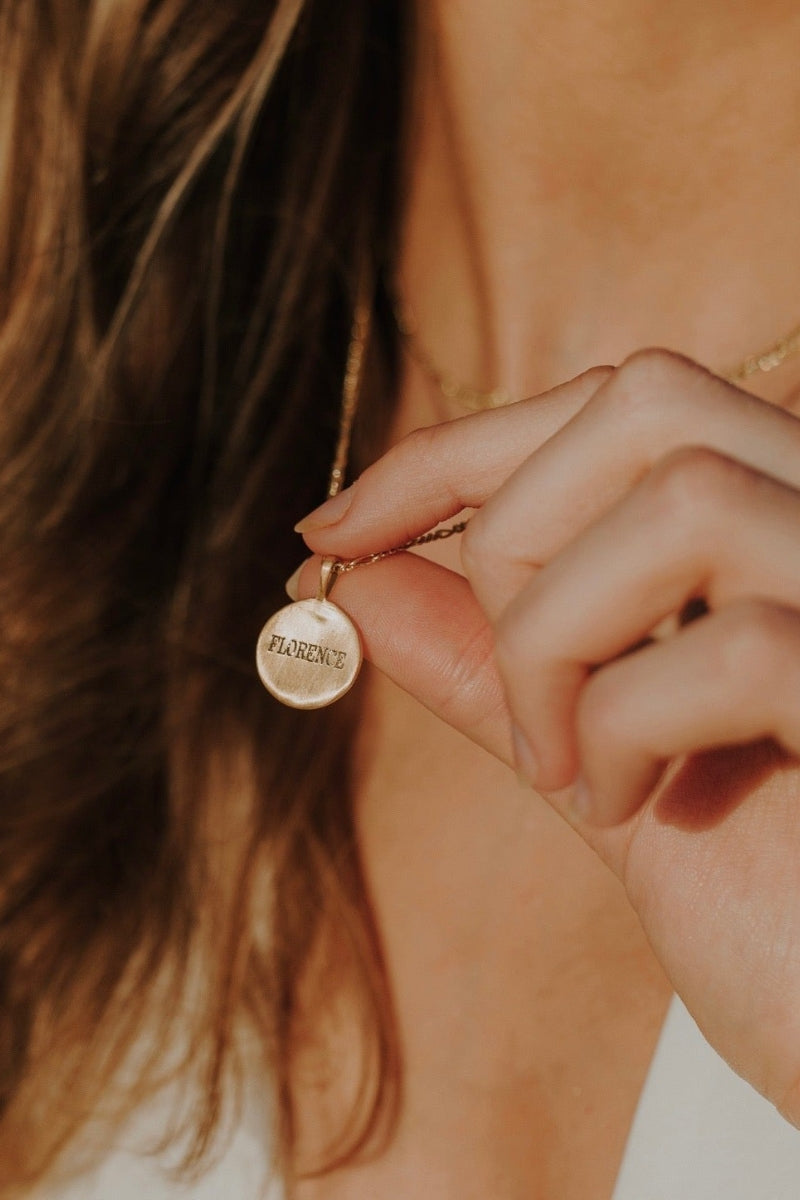 A Signature Necklace with Florence engraved on the front of the pendant is held out by the wearer to show the beautiful detailing on the pendant.