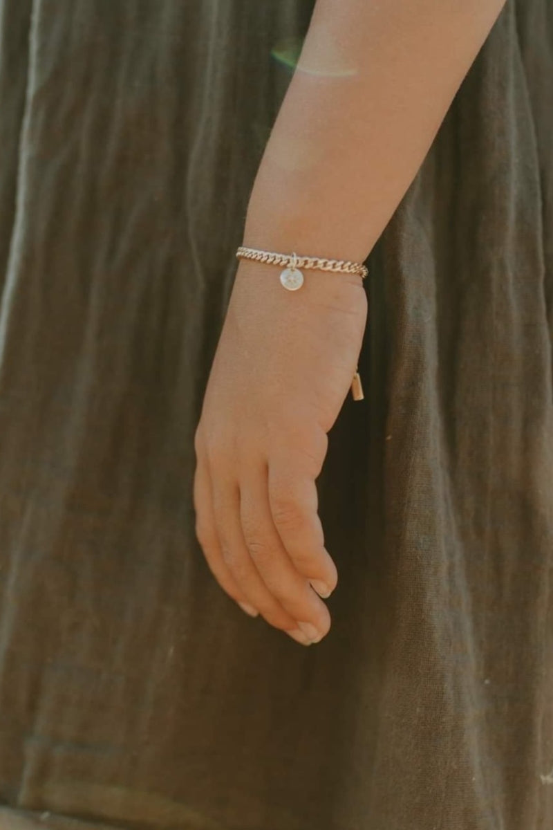 A young child wrist's wearing a gold Cuban Link Chain with a vintage pearl pendant crafted as timeless fine jewellery by Bluebird Co