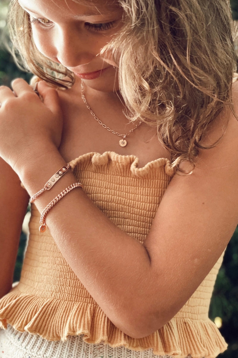 A young child wearing a rose gold Cuban Link Chain with a vintage pearl pendant and matching pearl bracelet, crafted as timeless fine jewellery by Bluebird Co
