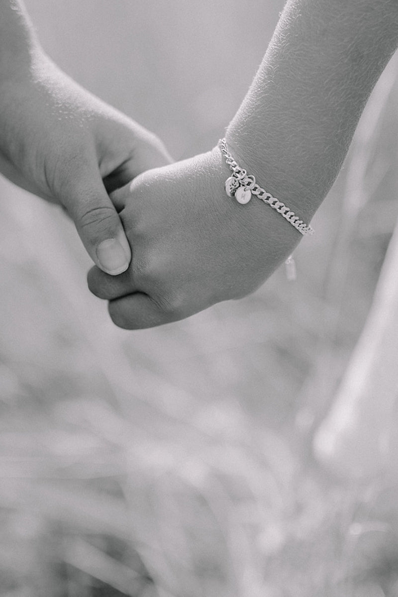 A close up image of a child's wrist wearing a Cuban Link Chain with a single vintage pearl pendant with a personalised solid gold initial pendant, crafted in elegant fine jewellery by Bluebird Co