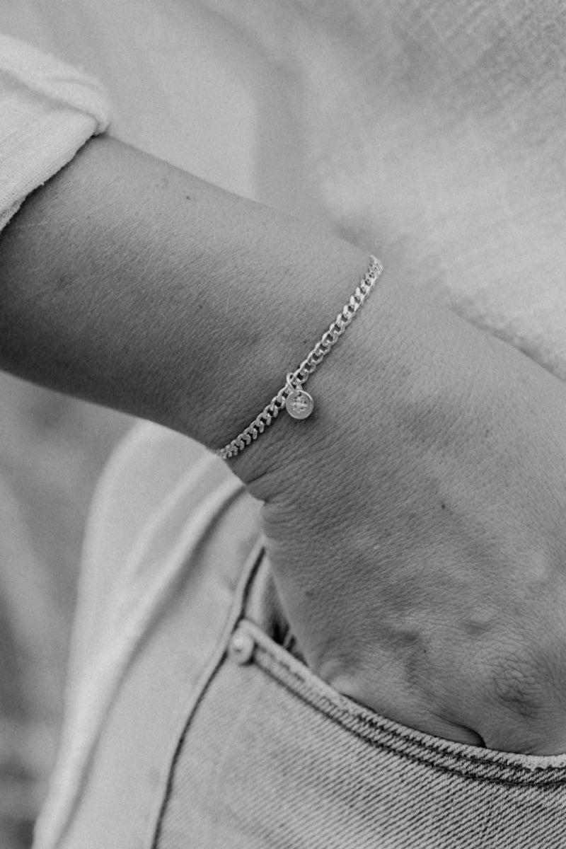 A close up image of a woman's wrist wearing a Cuban Link Chain with a single vintage pearl pendant, crafted in elegant fine jewellery