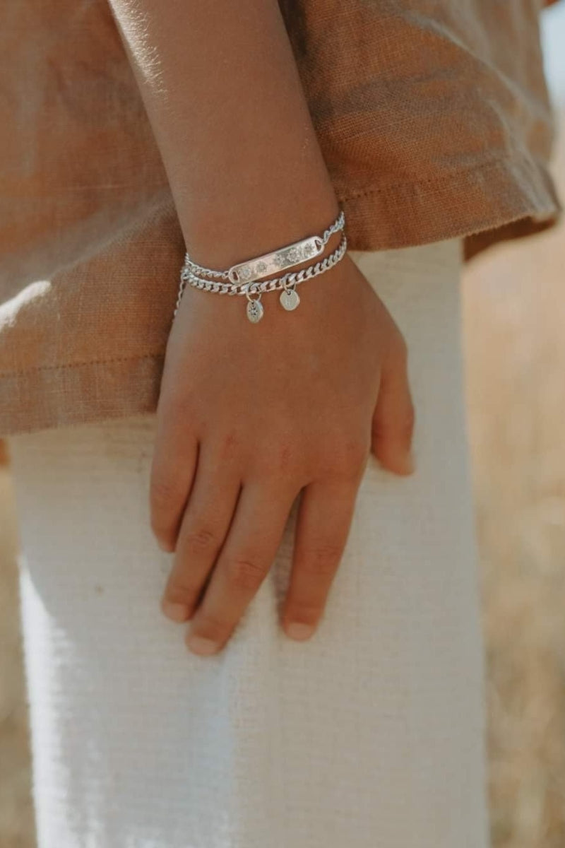 A detailed image of a young child's wrist wearing a Cuban Link Chain Necklace with a vintage pearl pendant and matching pearl bracelet, designed as a timeless keepsake.