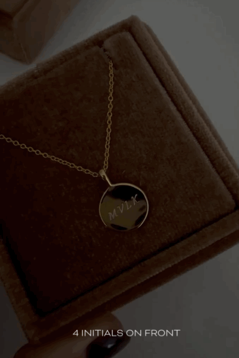 A gold Soleil Necklace is in a Blubeird Co brown velvet gift box and the shiny surface along with the engraving detail is shown on the necklace pendant.