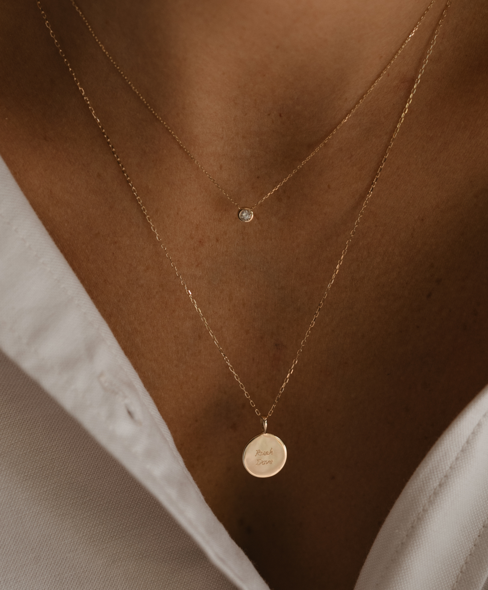 A woman is wearing a solid gold Lume necklace with the Soleil Pendant with personaliased engraving  on the front of the pendant.  It rests elegantly on a solid gold chain.