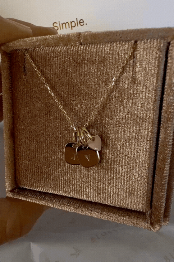 Bluebird Co's solid gold rectangular initial pendants stacked with a solid gold pink heart pendant on a solid gold necklace chain. 