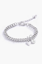 Silver chain bracelet with a heart-shaped tag and a mini inial pendant on a white background