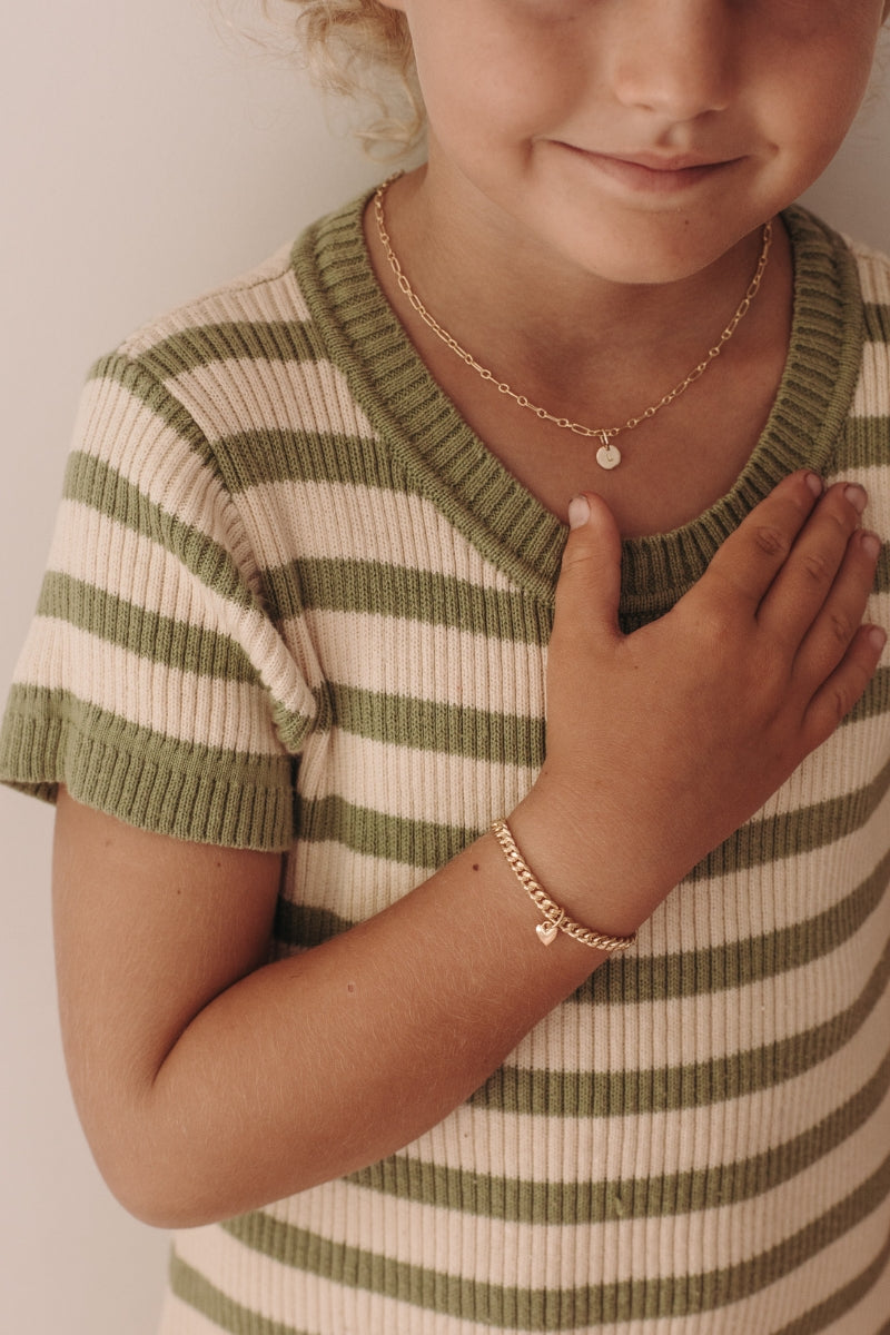 A young girl wearing the Sweetheart Cuban Link Chain Bracelet with a heart charm and a matching link chain necklace featuring an initial pendant, crafted in fine jewellery style by Bluebird Co