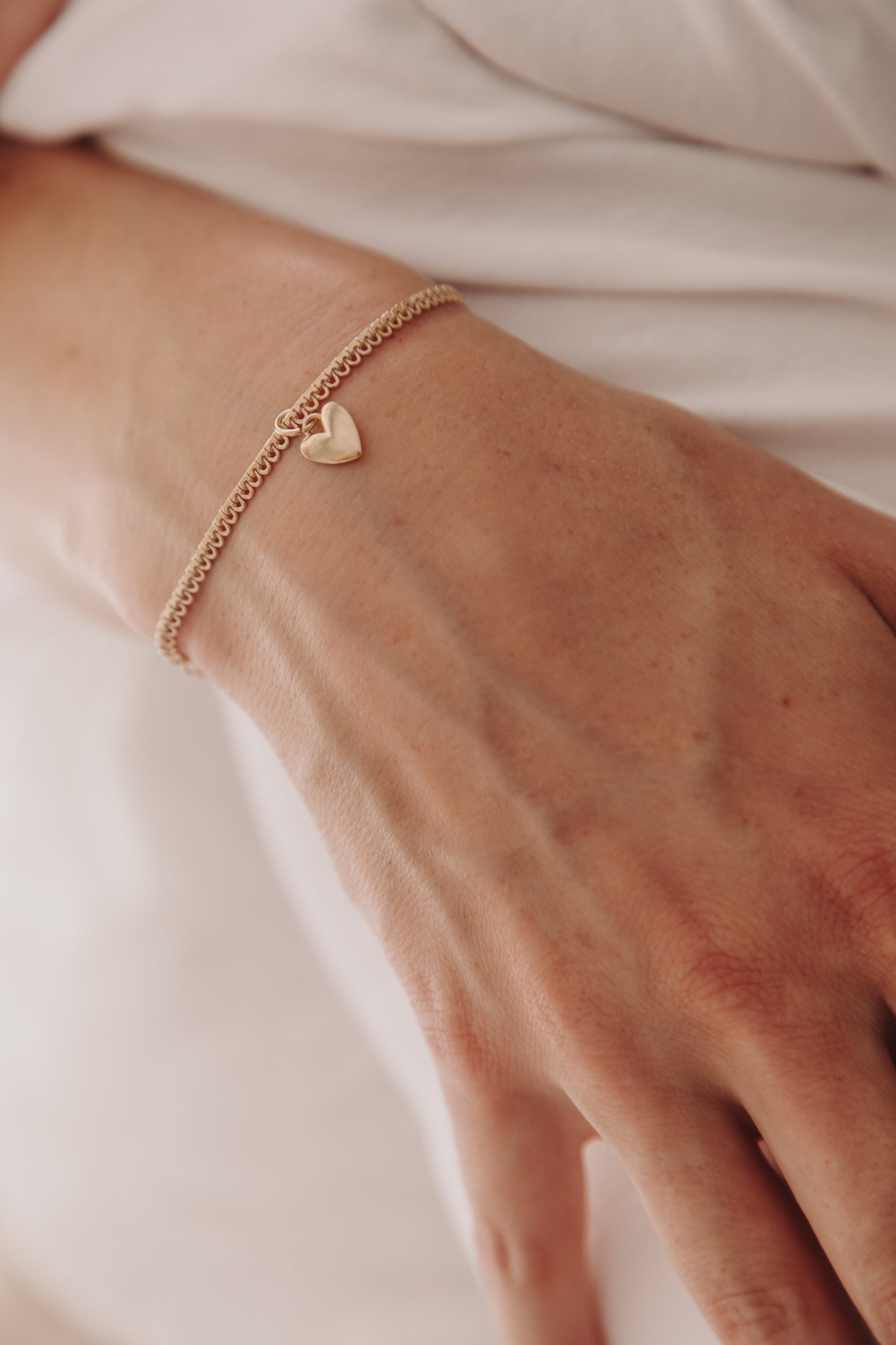 A close-up of a woman’s wrist adorned with the Sweetheart Lace Chain Bracelet and heart charm, designed as timeless minimalist jewellery.