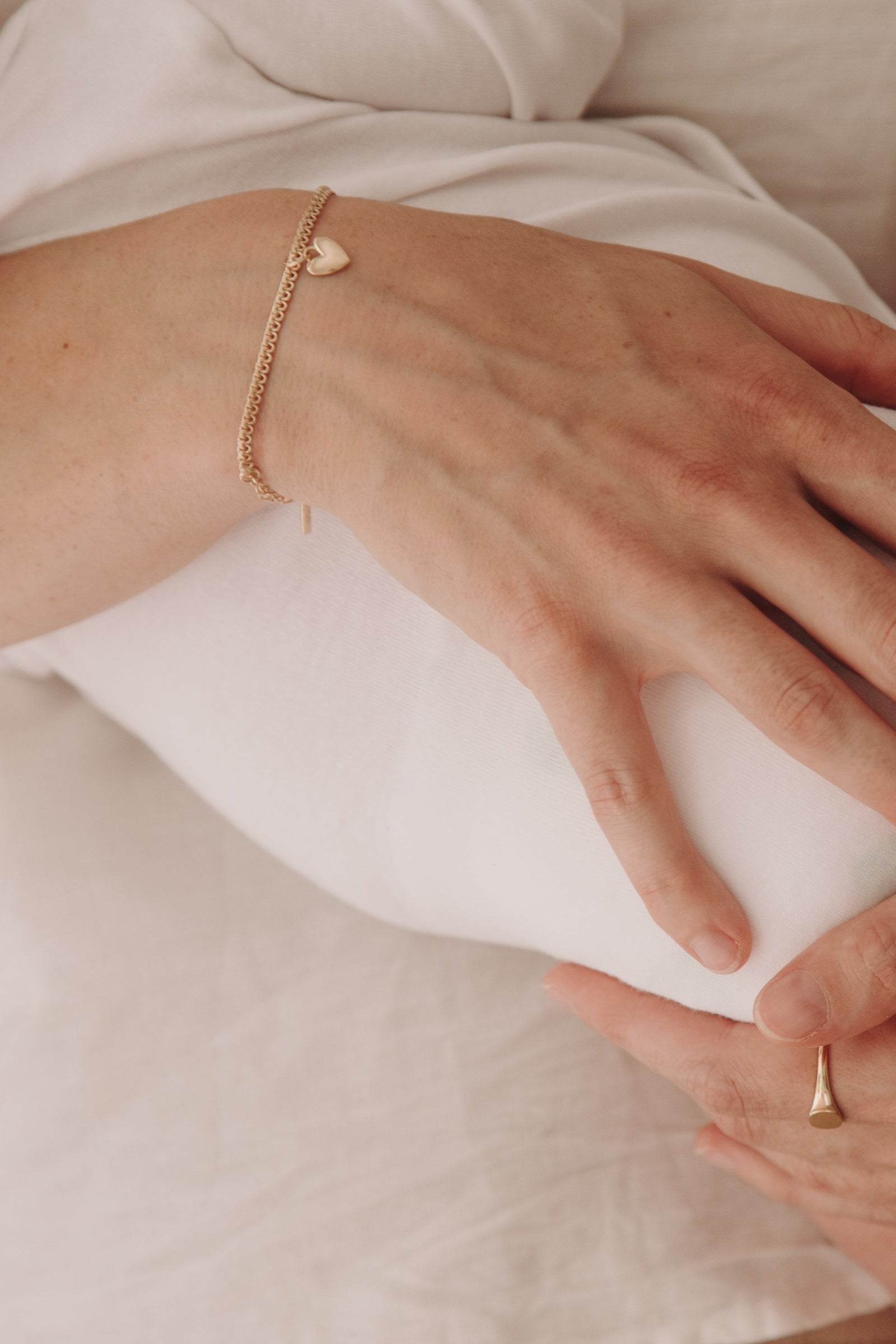 A close-up image capturing a woman holding a baby wearing a Lace Chain Bracelet with heart charm and matching gold signet ring, styled with refined simplicity by Bluebird Jewellery