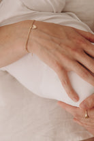 A close-up image capturing a woman holding a baby wearing a Lace Chain Bracelet with heart charm and matching gold signet ring, styled with refined simplicity.