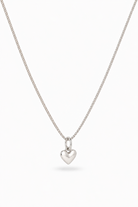 A delicate silver chain necklace with a small, polished heart-shaped pendant, displayed against a clean white background.