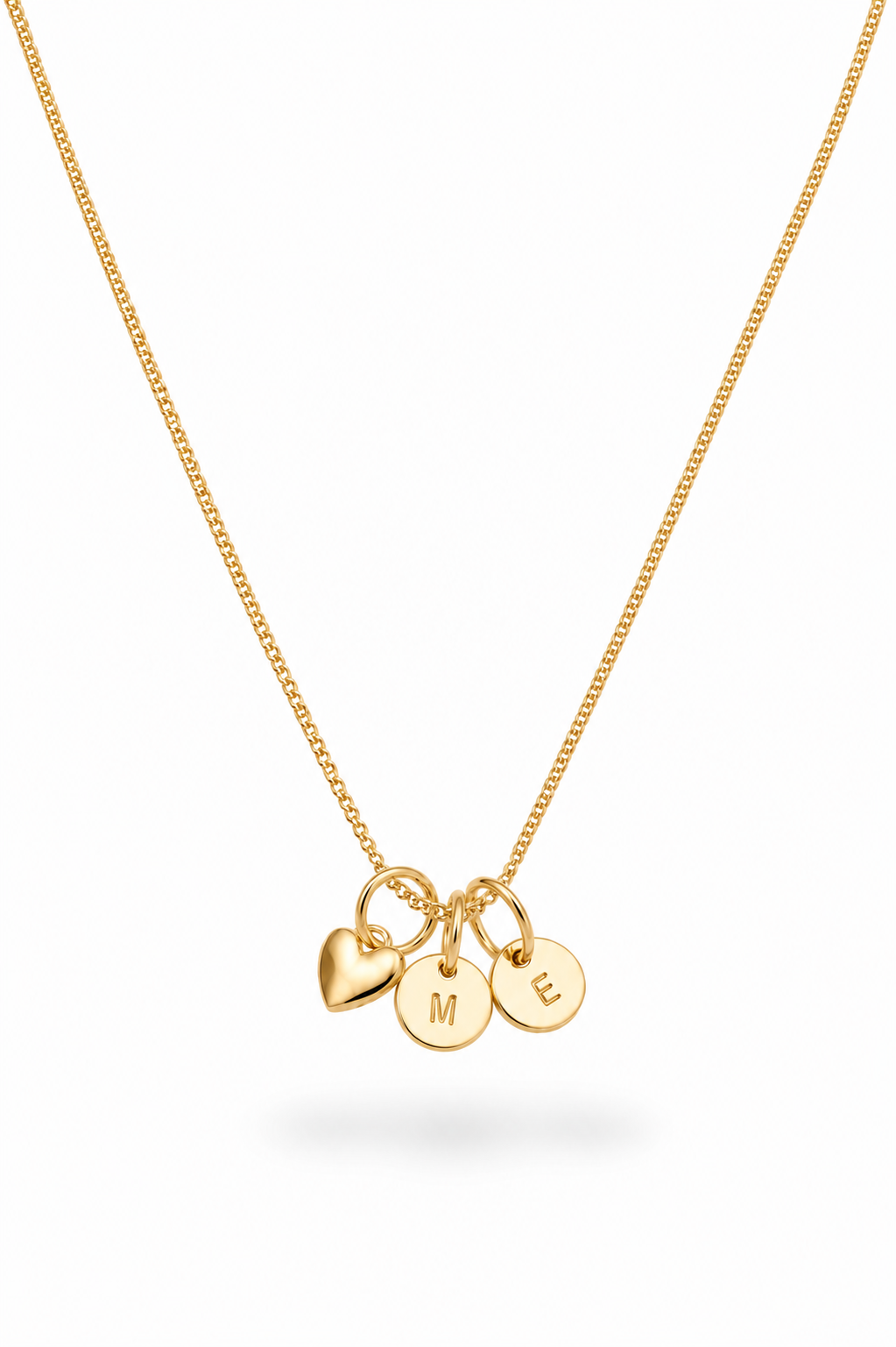 A delicate gold chain necklace featuring three small hanging charms: a heart, a disc engraved with the letter 'M', and a disc engraved with the letter 'E', shown on a clean white background.