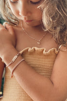 A close-up image of a child wearing the Darling Heart Bracelet by Bluebird Jewellery, showcasing five petite heart details within a refined and timeless gold chain.