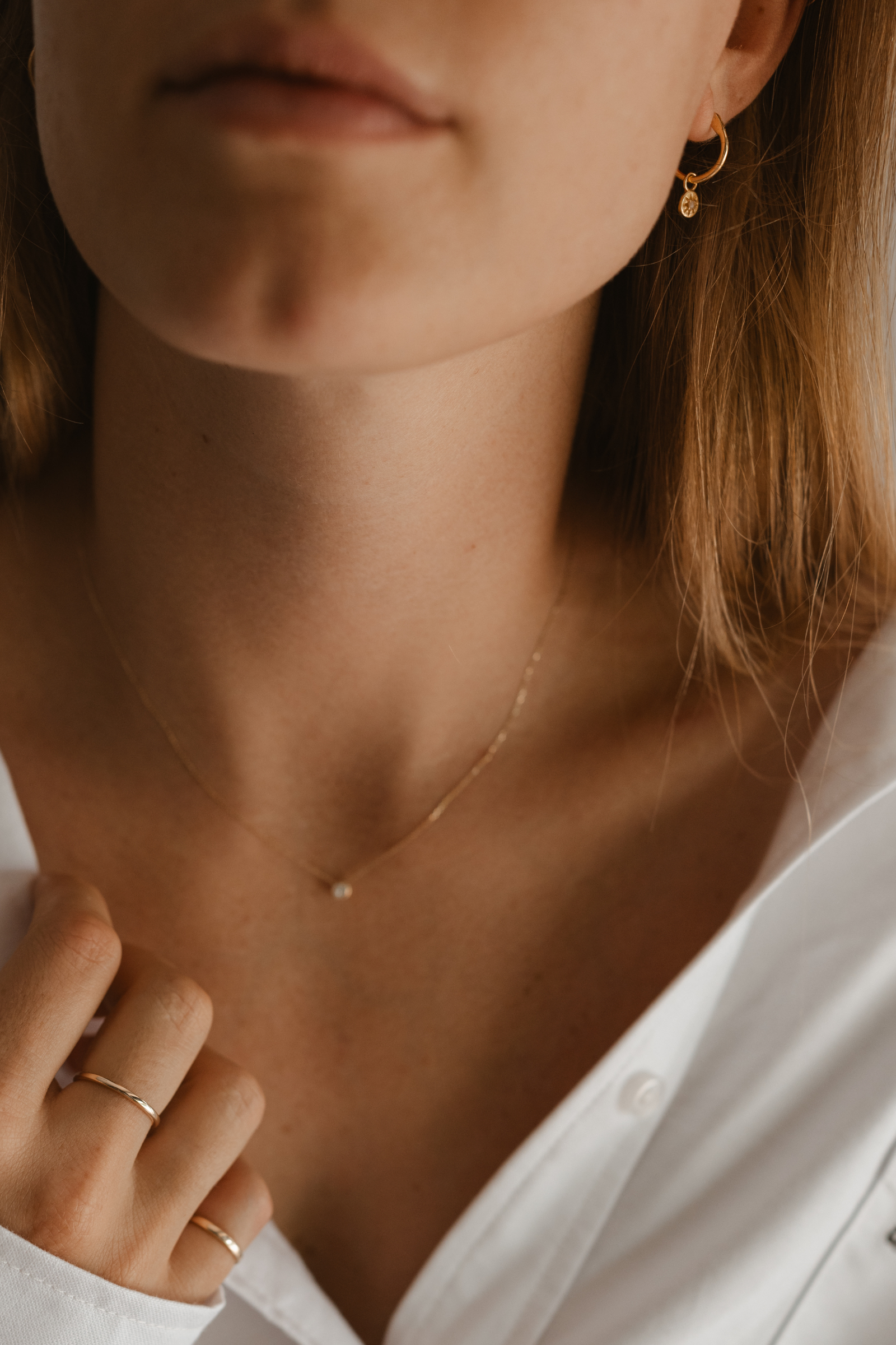 A woman is wearing The Petite Vintage Pearl Hoops with a crisp white shirt an find Signature Rings.  A timeless look.