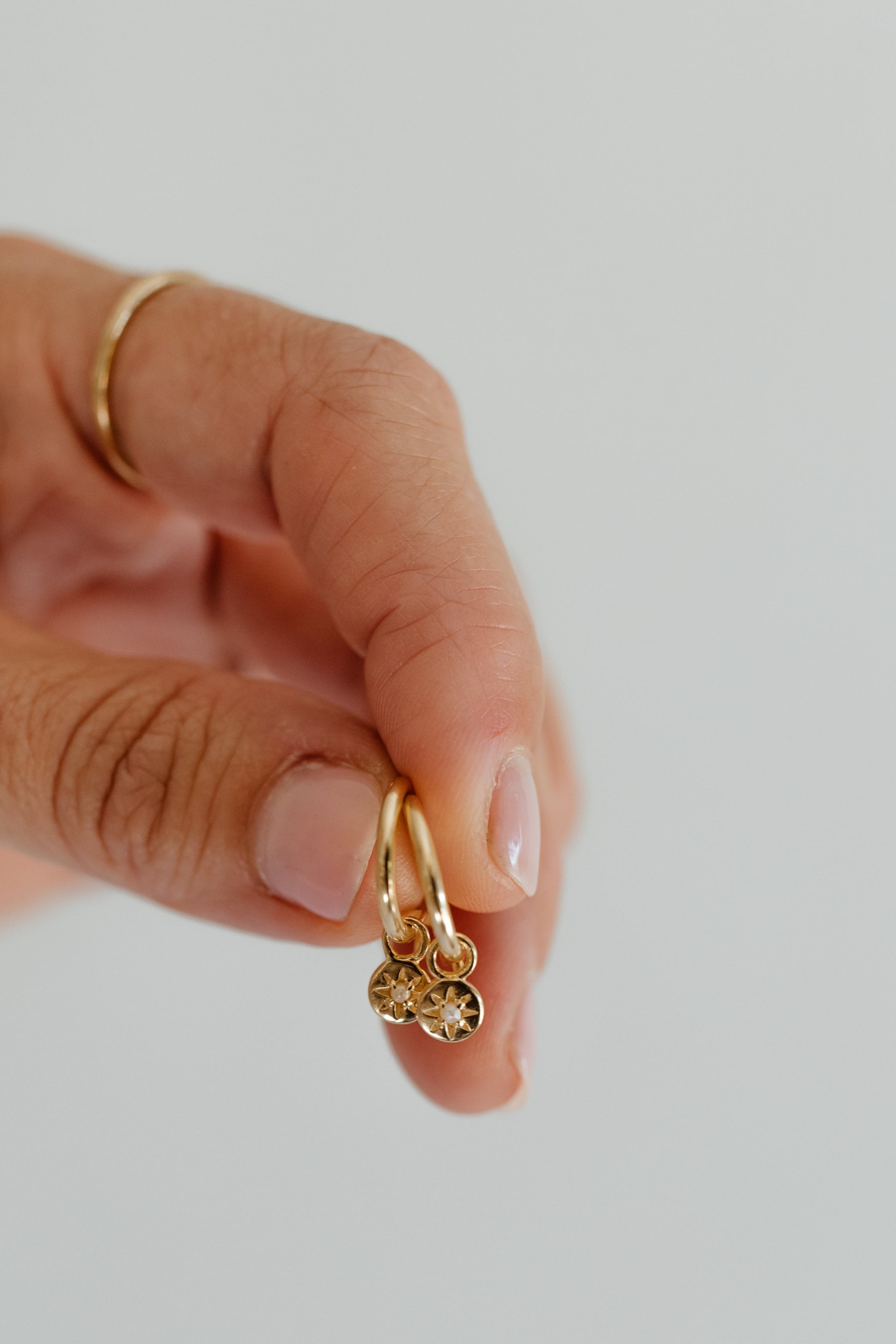 A pair of Petite Vintage Pearl Hoops are held in a hand up close.